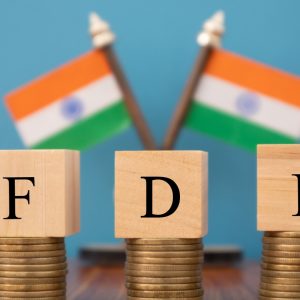 Concept of FDI or foreign Direct Investment on India in wooden block letters on stack of coins with Indian Flag as a background.
